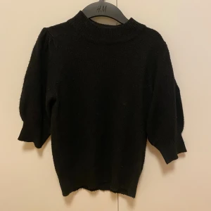 Svart stickad tröja från JDY - Svart stickad tröja från JDY med halvpolo och kortare puffärmar. Tröjan har ribbade muddar vid hals, ärmslut och nederkant. Bra skick!