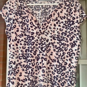 Leopardmönstrad topp L - Säljer en snygg topp från RoseBud med rosa och svart leopardmönster. Toppen har v-ringning och korta ärmar, perfekt för dig som vill sticka ut lite extra. Mjuk och skön i materialet, passar till många olika stilar.