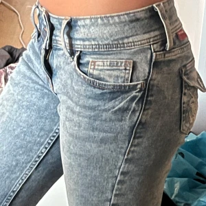 Ljusblå lågmidjade bootcut jeans - Säljer ett par ljusblå jeans med bootcut passform och låg midja. Jeansen har snyggt tvättad denim, dubbla knappar i midjan och en broderad bakficka med knappar. Klassisk femficksmodell och coola detaljer som gör dem unika. Dessa bilder är tagna av en annan person och säljer dessa igen då jeansen var för korta för mig. Priset kan diskuteras.💗
