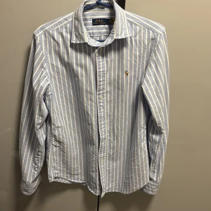 Polo Ralph Lauren skjorta - Pris kan diskuteras!  Snygg blå och vit randig skjorta från Polo Ralph Lauren med klassisk krage och broderad logga på bröstet. Perfekt för en clean och stilren look.