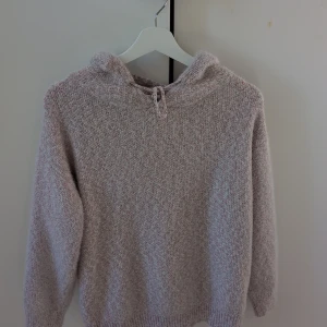 Ljusrosa stickad hoodie från Silverswan - Supermjuk och fluffig stickad hoodie i ljusrosa och vitt från Silverswan. Tröjan har huva med snörning och långa ärmar, perfekt för kyliga dagar. Ribbstickade muddar vid ärmslut och nederkant ger en skön passform.