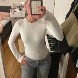 Vit långärmad bodysuit från Zara - Säljer en vit långärmad bodysuit från Zara med rund hals och en riktigt snygg öppen rygg. Tight passform och stretchigt material som sitter som en smäck. Perfekt att styla med jeans eller kjol för en clean look. Använd 1 gång 