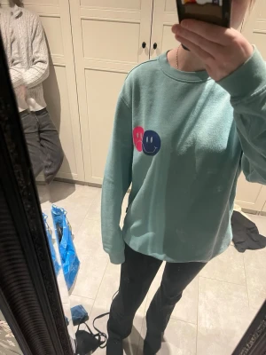 Turkos sweatshirt från WINWIN - Säljer en turkos sweatshirt från WINWIN i storlek M. Tröjan har en relaxed fit och tryck med två smileys i rosa och blått på bröstet. Mjuk insida och rund halsringning. Perfekt för dig som gillar streetwear och färgglada detaljer. Pris diskuteras gärna! 