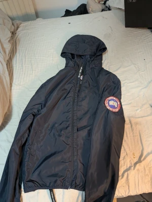 Canada goose vindjacka - Här har vi en skön vindjacka från Canada goose riktigt fin på storlek 165/175, kommer i Canada goose förpackning riktigt fint, bra skick förutom märket på ärmen de är helt okej skick som man kan se inte topp liksom.