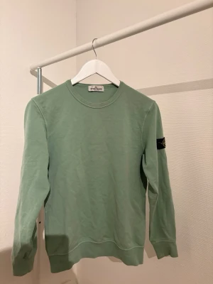 Grön sweatshirt från Stone Island - Snygg ljusgrön sweatshirt från Stone Island med klassisk rund hals och ribbade muddar. Tröjan har den ikoniska svarta patchen med gul kompasslogga på vänster ärm. Tillverkad i mjuk bomull för en skön och avslappnad stil. Perfekt till kommande våren. Priset är ej fast, det går att pruta. Tveka inte på att fråga kring funderingar!