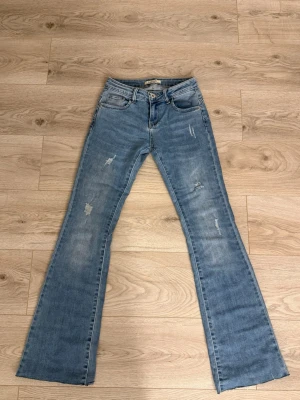 Ljusblå  bootcut jeans med slitningar - Snygga ljusblå bootcut jeans med slitna detaljer och klassisk femficksmodell. Jeansen har låg midja och är tillverkade i mjukt denimtyg som ger en avslappnad vibe och är figursydd upptill. Perfekta för dig som gillar en retroinspirerad look.