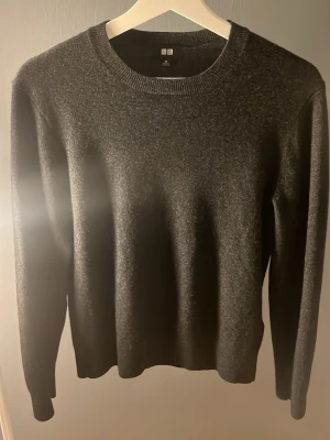 Mörkgrå Kashmir tröja från uniqlo - Mysig mörkgrå stickad tröja från Uniqlo med rund halsringning och långa ärmar. Tröjan har en enkel och stilren design, perfekt för lager på lager. Materialet känns mjukt och skönt mot huden.