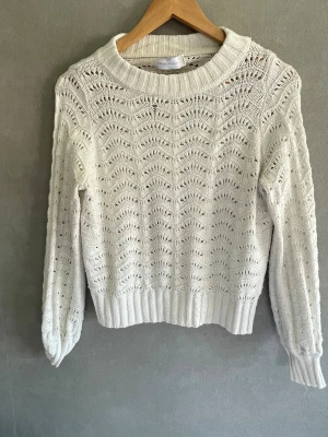 Vit stickad tröja med hålmönster - Snygg vit stickad tröja från Gina Tricot med ett detaljerat hålmönster i hela plagget. Tröjan har rund halsringning, ribbade muddar och avslut. Tillverkad i mjukt material som känns skönt mot huden. Perfekt för lager på lager och en fräsch look.