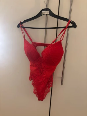Röd spetsbody från H&M - Snygg röd body från H&M med tunna axelband och vadderade kupor. Bodyn är dekorerad med spetsdetaljer framtill och har en djup urringning. Materialet är mjukt och stretchigt för en bekväm passform. Perfekt för dig som vill känna dig extra fin. Priser kan diskuteras