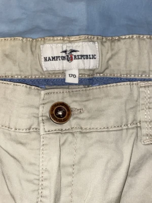 Beige chinos från Hampton Republic - Snygga beige chinos från Hampton Republic med klassisk passform. Byxorna har detaljerade sömmar, knapp med logga och broderad logotyp ovanför bakfickan. Perfekta för en stilren och avslappnad look.