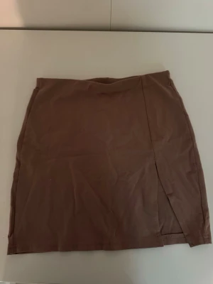 Brun kjol från SHEIN - Säljer en enkel och snygg brun/beige kjol från SHEIN. Kjolen är kort och har en stilren design med slits framtill. Perfekt att matcha med en crop top eller stickad tröja för en trendig look.🤎