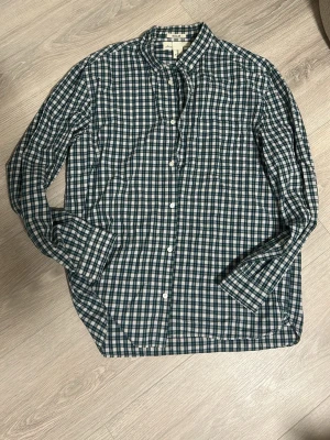 Grön och vit rutig skjorta  - Snygg långärmad skjorta från H&M grönt och vitt rutigt mönster. Skjortan har klassisk krage, knäppning framtill och bröstficka. Perfekt för en avslappnad men stilren look.