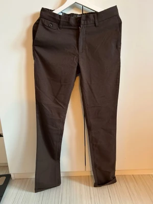 Dressmann Slim Fit Flannel Stretch Chinos - Dessa helt nya chinos med etikett i storlek 28/32 är det perfekta tillskottet till en snygg men avslappnad garderob (smart-casual). Byxorna kommer i en fyllig mörkbrun färg och erbjuder en bekväm passform tack vare resår baktill i midjan och ett mjukt flanell-liknande tyg med extra stretch. 