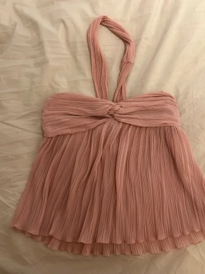 Plisserad rosa halterneck topp - Supersöt plisserad rosa halterneck topp med twistad detalj framtill. Toppen har en flowy passform och tunna axelband som knyts i nacken. Perfekt för dig som vill ha en feminin och trendig look.💝💝