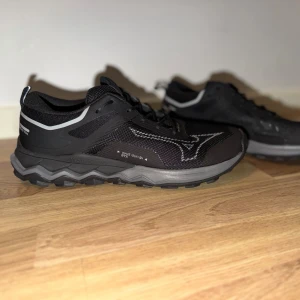 Svarta Mizuno Gore-Tex sneakers med reflexdetaljer - Använda i ca1 timme. Snygga svarta sneakers från Mizuno med grå och vita reflexdetaljer. Skorna har en robust sula med grovt mönster för extra grepp och ovandel i mesh för bra ventilation. Perfekta för dig som gillar sportig stil och vill ha bekväma skor till vardags.