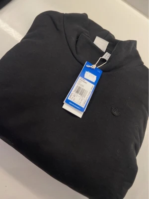 cropped Svart hoodie från Adidas Originals - Säljer en svart hoodie från Adidas Originals med den klassiska Trefoil-loggan broderad på bröstet. Hoodien har en enkel och clean design med huva och långa ärmar. Tillverkad i mjukt material som känns skönt mot huden.  Cropped 