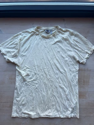 Benvit t-shirt från Reclaimed vintage strl M - En enkel och stilren benvit t-shirt från Reclaimed vintage. T-shirten har rund halsringning och korta ärmar. Tillverkad i mjuk bomull som känns skön mot huden. Perfekt basplagg att matcha med jeans eller shorts.