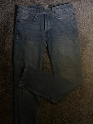 Dressman  blå jeans straight fit - Klassiska blå dressman jeans med rak passform och femficksmodell. Jeansen har normal midja och är tillverkade i slitstarkt bomullsdenim. Perfekta för dig som gillar tidlös stil och vill ha ett par riktigt schyssta jeans i garderoben.