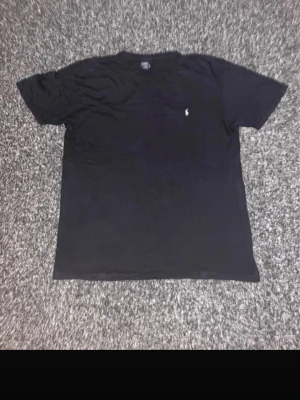 Svart t-shirt från Ralph Lauren - Klassisk svart t-shirt från Ralph Lauren med den ikoniska lilla loggan broderad på bröstet. T-shirten har rund halsringning och korta ärmar. Bara att fråga vid funderingar 