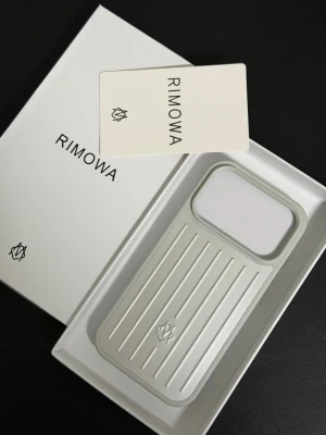 Rimowa iPhone 17 Pro silverfärgat mobilskal - Snyggt och stilrent mobilskal från Rimowa i silverfärgad aluminium med klassisk räfflad design. Skalets insida är fodrad för extra skydd och har en öppning för kamera. Passar perfekt för dig som vill ha ett exklusivt och tåligt skal till din iPhone.