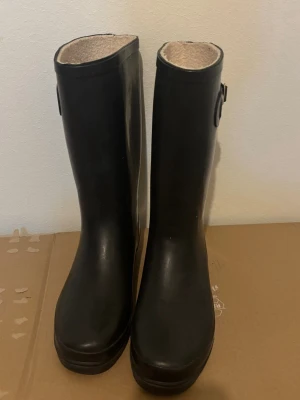Gummistövlar  - Svarta gummistövlar med spänne på sidan och mjukt foder på insidan. Perfekta för regniga dagar.