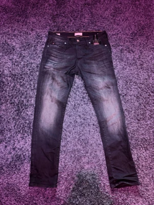 Mörka Jacknjones jeans med slim passform - Snygga mörkblå jeans från jacknjones  med diskreta slitningar och klassisk femficksdesign. Jeansen har en slim passform och raka ben, perfekt för en stilren look. Materialet är mjukt och stretchigt jeans för extra komfort.