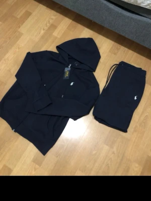 Mörkblå -set från Polo Ralph Lauren - Snyggt mörkblått set från Polo Ralph Lauren med zip-hoodie och matchande byxor. Setet har den klassiska loggan broderad på både tröjan och byxorna. Perfekt för chill dagar hemma eller när du vill vara bekvämt stylish. Mjukt material och avslappnad passform.Använd ett fåtal gånger!