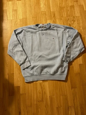 Ljusblå sweatshirt från Tommy Hilfiger - Ljusblå sweatshirt från Tommy Hilfiger med liten broderad logga på bröstet. Klassisk rund halsringning och ribbade muddar vid ärmslut och nederkant. Mjuk insida och diskreta detaljer i rött, vitt och blått vid nacken.