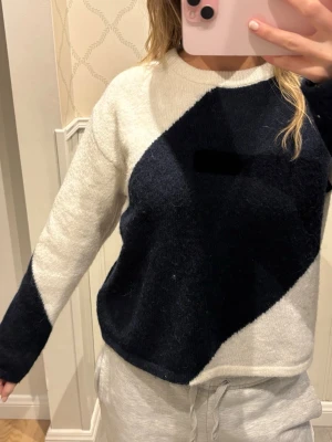 Stickad tröja med svartvit design - Säljer en stickad tröja med unik diagonal färgblock-design i svart och vitt. Tröjan har rund halsringning och långa ärmar. Perfekt för dig som gillar en modern och stilren look. Materialet känns mjukt och bekvämt mot huden.