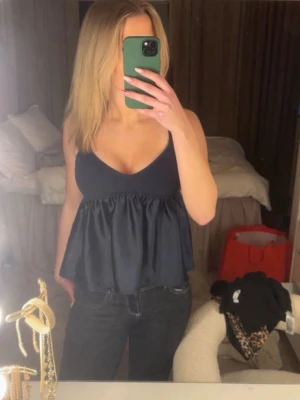 Mörkblå linnetopp från Storets - Supersöt mörkblå linnetopp från Storets med smala axelband och v-ringning. Överdelen är ribbad och underdelen har ett glansigt, utsvängt tyg som ger en flowy känsla. Perfekt att styla med jeans eller kjol.