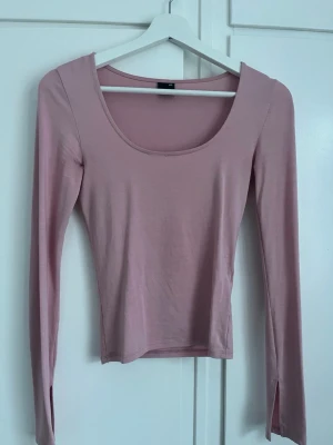 Ljusrosa långärmad topp med rund hals - Säljer en ljusrosa långärmad topp med djup rundringning och figurnära passform. Tillverkad i mjukt, stretchigt material som känns skönt mot huden. Perfekt att styla med jeans eller kjol för en enkel och snygg look.