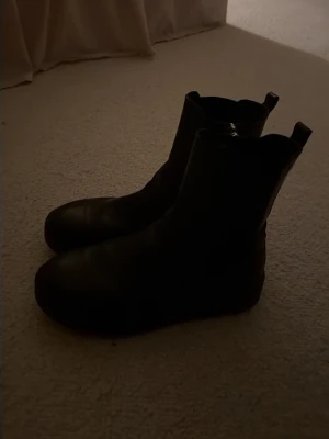 Svarta chelsea boots i skinn - Stilrena svarta chelsea boots med klassisk rund tå och resår på sidorna. Tillverkade i skinn och har en platt sula. Perfekta för dig som vill ha en tidlös och enkel look.