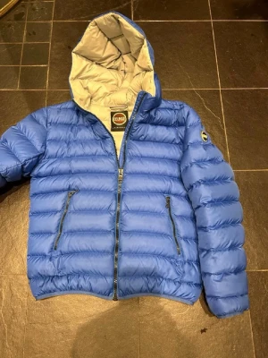 Blå dunjacka med huva från Colmar - Snygg blå dunjacka från Colmar med huva och dragkedja framtill. Storlek M men passar S(48). Jackan har två dragkedjeförsedda fickor och ett ljust innerfoder. Perfekt för kalla dagar och enkel att matcha med olika outfits.  Pris e diskuterbart!