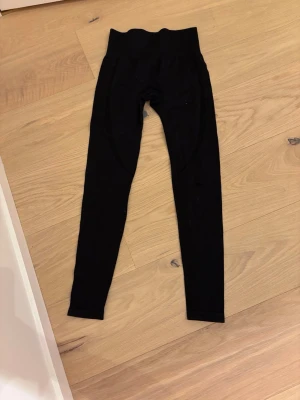 Svarta ribbade leggings med hög midja - Svarta leggings med ribbad struktur och hög midja. Stretchigt material som sitter tight och formar sig efter kroppen. Perfekta till en avslappnad look eller till träning. Klassisk modell utan synliga loggor.