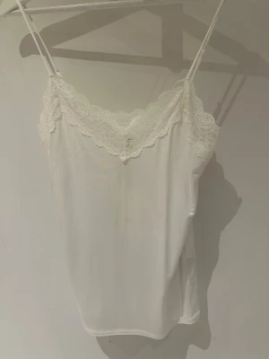 Vit spetslinnetopp från Object storlek S/M - Säljer en vit linnetopp från Object med tunna axelband och vacker spetsdetalj längs urringningen. Toppen har en mjuk och lätt känsla, perfekt för lager på lager eller sommarens varma dagar. Enkel och stilren design som passar till mycket.