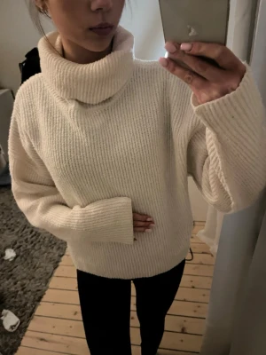 Beige stickad polotröja - Mysig beige stickad polotröja med grov ribbstickning och oversized passform. Tröjan har långa ärmar och en hög, bred polokrage som ger en avslappnad och trendig look. Perfekt för kalla dagar och enkel att styla med jeans eller leggings.