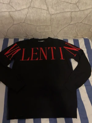 Svart stickad tröja från Valentino - Svart stickad tröja från Valentino med stor röd logotyp över bröstet och axlarna. Tröjan har rund hals, långa ärmar och ribbade muddar. Materialet är mjukt och känns lyxigt.