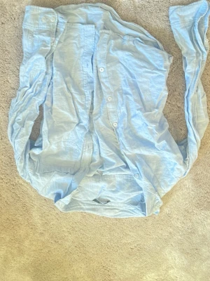 Ljusblå skjorta från Ellos - Säljer en ljusblå skjorta från Ellos i storlek 170. Skjortan har klassisk krage, långa ärmar och knappar framtill. Materialet är linne vilket gör den skön och luftig. Perfekt för dig som gillar en enkel och stilren look.