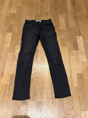 Levi's 512 Slim Taper svarta jeans - Svarta Levi's 512 Slim Taper jeans med klassisk femficksdesign och smal, avsmalnande passform. Jeansen har en mörk tvätt och är tillverkade i mjukt jeansmaterial med knapp och dragkedja framtill. Perfekta för dig som gillar en modern och stilren look.