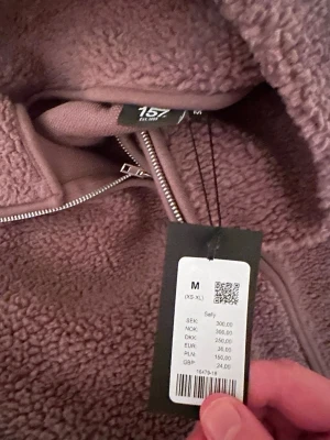 Brun teddyjacka från lager 157 i storlek M - Mysig brun teddyjacka från 157 med hel dragkedja framtill och hög krage. Jackan är tillverkad i 100% polyester och har en loose fit med långa ärmar. Perfekt för kalla dagar när du vill vara både varm och snygg.