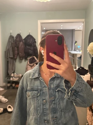 Blå jeansjacka från Gina Tricot - Säljer en klassisk blå jeansjacka från Gina Tricot med snygga silverfärgade knappar framtill och två bröstfickor med lock. Jackan har en rak passform och är långärmad, perfekt att slänga på över en hoodie eller t-shirt.