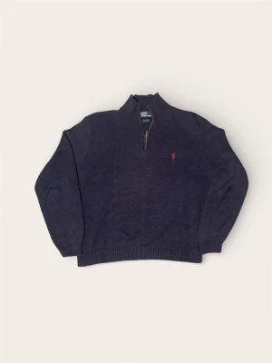 Mörkblå stickad tröja Polo Ralph Lauren - Snygg mörkblå stickad tröja från Polo Ralph Lauren i 100% bomull. Tröjan har half zip med metallblixtlås och en liten röd logga broderad på bröstet. Ribbstickade muddar vid ärmslut och nederkant ger en schysst passform. Perfekt för kyliga dagar.