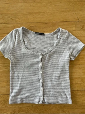 Gråvit randig topp från Brandy Melville - Säljer en kortärmad topp från Brandy Melville i grått och vitt med smala ränder. Perfekt skick utan defekter