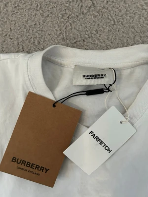 Vit burberry t-shirt  - Vit t-shirt från Burberry med klassisk svart logotyp 'BURBERRY LONDON ENGLAND' tryckt på bröstet. Rund halsringning och korta ärmar. Tillverkad i mjuk bomull för en skön känsla. Perfekt för dig som gillar stilrena designer och ikoniska märken.Aktiv 24/7✅ Skickas inom 24h📦🚚 Kan gå ner i hugget 😃✅ Hör av er via frågor⁉️