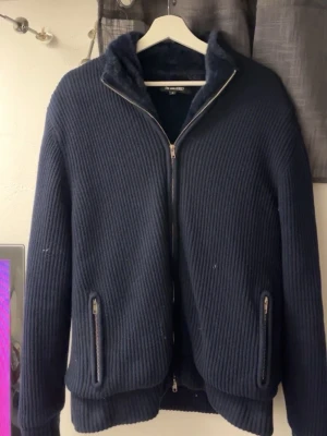 Mörkblå teddyjacka från The Gallerist - Mysig mörkblå teddyjacka från The Gallerist i storlek S. Jackan har ribbad yta, fluffigt foder, två fickor med dragkedja och hel dragkedja framtill. Perfekt för kyliga dagar och har en clean, modern look.