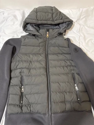 Moncler cardigan i svart mörkgrå färg hybridjacka - Säljer en stilren Moncler hybridjacka i en snygg mörkgrå färg. Modellen kombinerar en varm quiltad framsida med bekväma stickade ärmar och baksida. Priset kan diskuteras vid snabb affär 