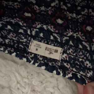 Mönstrad kortklänning från Hollister - Supersöt kortklänning från Hollister med smala axelband och ett blått, vitt och rött geometriskt mönster. Klänningen har en figurnära passform upptill och ett lätt utställt kjolparti. Perfekt för varma dagar och har en ungdomlig vibe. Egentligen shorts nertill