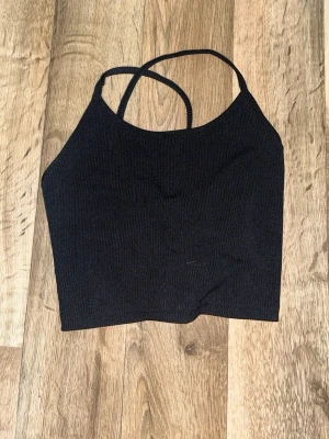 Svart croppad linnetopp med snörning - Säljer en svart croppad linnetopp med tunna axelband och snygg snörning i ryggen. Toppen är ribbad och har en stilren, enkel design som passar perfekt till jeans eller kjol. Materialet känns mjukt och stretchigt mot huden. Använd ett fåtal gånger och är från SHEIN 