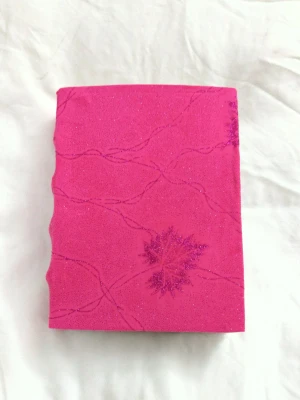 Handgjord anteckningsbok med rosa glittrigt omslag - Denna unika anteckningsbok har ett handgjort, rosa glittrigt omslag med blommönster och handgjort papper. Perfekt för dig som vill skriva, rita eller skapa egna berättelser. De tjocka, vita sidorna ger en kreativ känsla och gör boken extra speciell. Passar dig som gillar att sticka ut och vara kreativ! A5 storlek ca 100 sidor