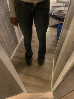 Bootcut jeans  - Säljer ett par bootcut jeans i mörkblå denim med klassisk femficksdesign. Jeansen har låg midja och är tillverkade i bomullsmaterial. Benen är något utsvängda och har slitna detaljer längst ner vid bensluten för en cool look.